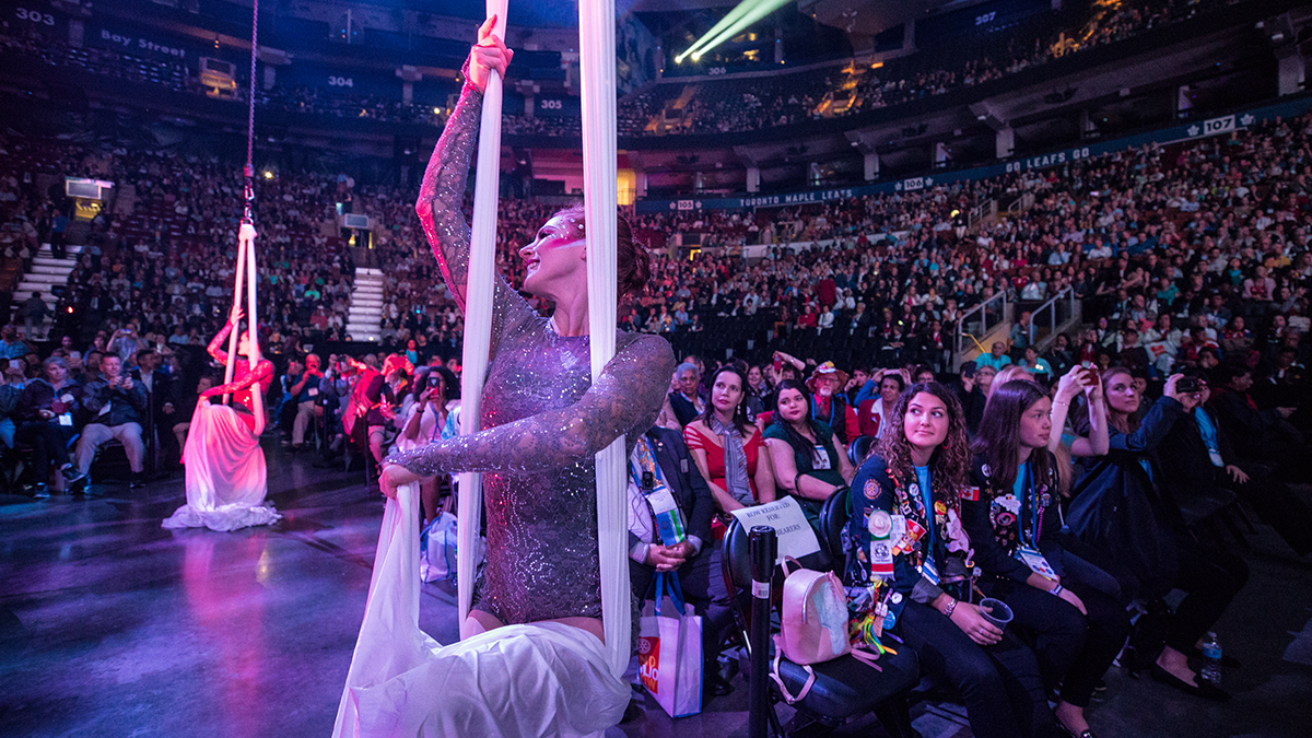 Un groupe de participants à la convention assis regarde des danseurs se produire pendant une séance plénière.
